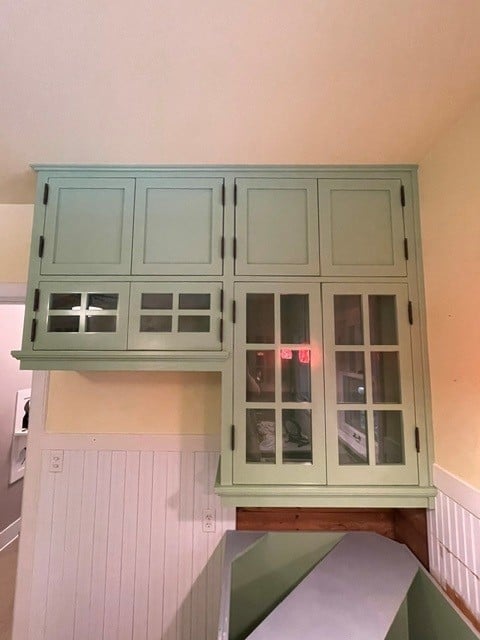 Vintage sage green wooden cabinet with glass doors and paned windows mounted on a peach-colored wall in a home interior