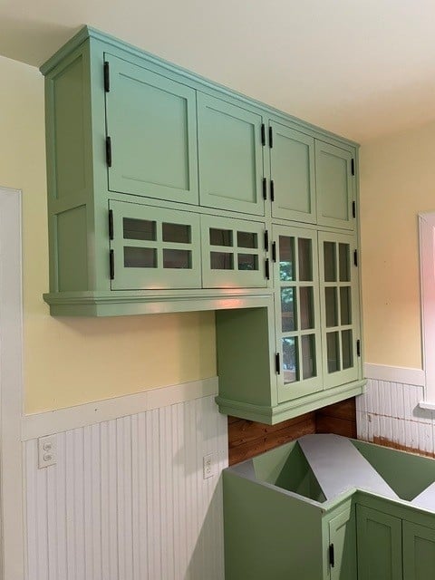 Sage green kitchen cabinetry with glass-front doors and black hardware